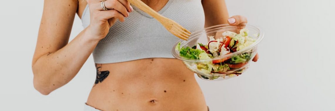 Young woman in sports attire holding a fresh salad bowl, promoting a healthy lifestyle.